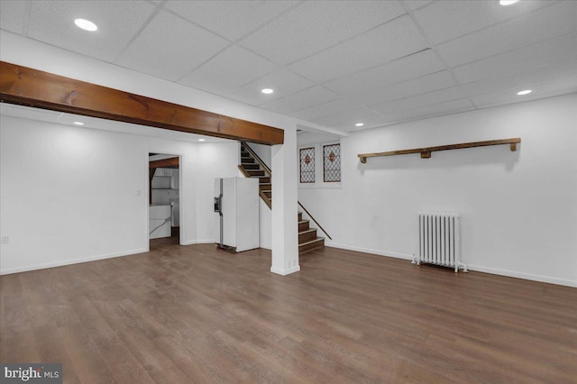 basement featuring a paneled ceiling, radiator heating unit, and hardwood / wood-style flooring