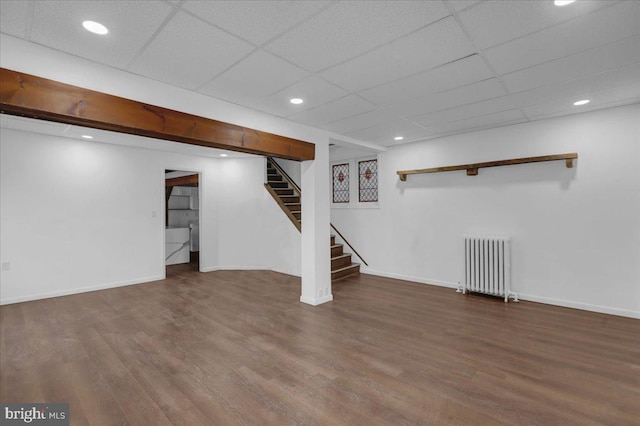 basement featuring a drop ceiling, wood-type flooring, and radiator heating unit