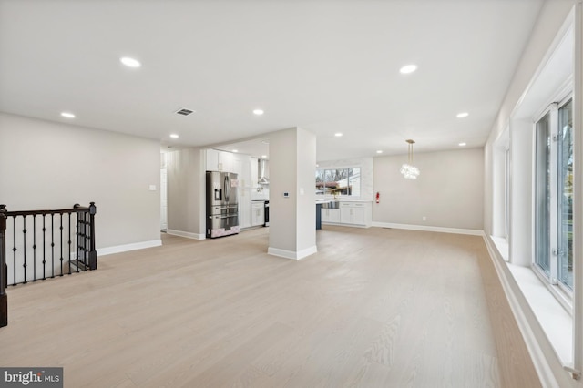 basement featuring stainless steel refrigerator with ice dispenser, light hardwood / wood-style floors, and an inviting chandelier