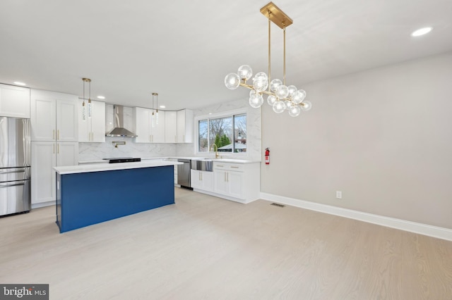 kitchen featuring appliances with stainless steel finishes, white cabinetry, hanging light fixtures, and wall chimney range hood