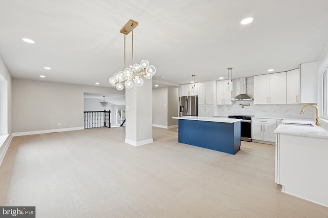 kitchen featuring white cabinetry, sink, a center island, wall chimney range hood, and appliances with stainless steel finishes