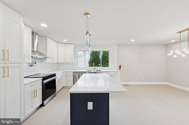 kitchen featuring a center island, stainless steel appliances, wall chimney range hood, pendant lighting, and white cabinets