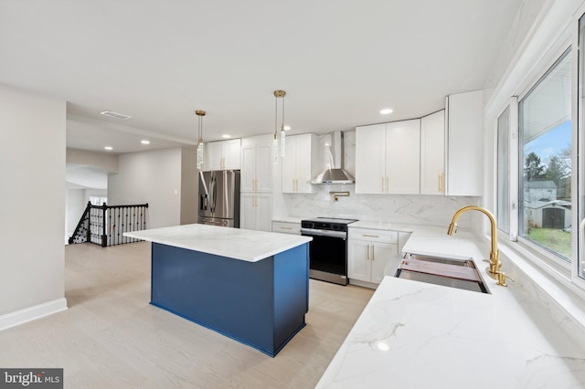 kitchen featuring appliances with stainless steel finishes, wall chimney exhaust hood, sink, white cabinetry, and hanging light fixtures