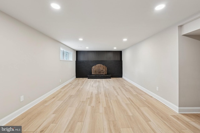 basement featuring a brick fireplace and light hardwood / wood-style flooring