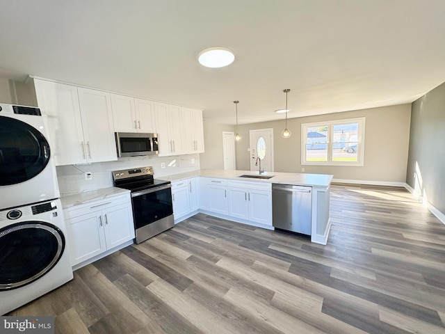 kitchen with stainless steel appliances, kitchen peninsula, stacked washer / drying machine, decorative light fixtures, and white cabinets