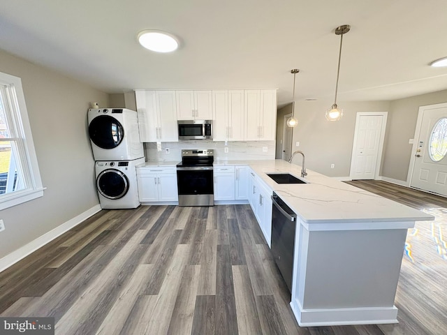 kitchen featuring kitchen peninsula, appliances with stainless steel finishes, sink, decorative light fixtures, and stacked washer and dryer