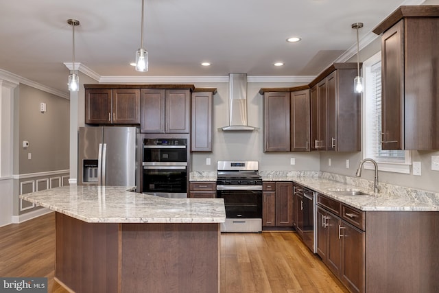 kitchen with pendant lighting, wall chimney range hood, sink, light wood-type flooring, and appliances with stainless steel finishes