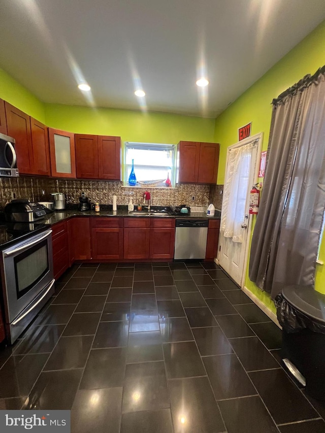 kitchen with appliances with stainless steel finishes, tasteful backsplash, dark tile patterned flooring, and sink