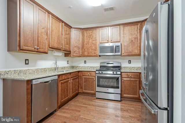 kitchen featuring stainless steel appliances, sink, light hardwood / wood-style flooring, and light stone countertops