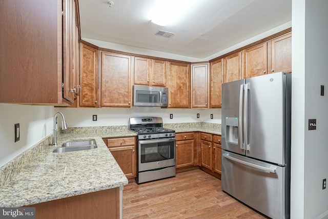 kitchen featuring kitchen peninsula, sink, light wood-type flooring, stainless steel appliances, and light stone counters