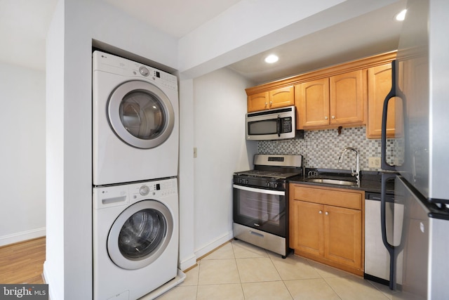 kitchen with appliances with stainless steel finishes, tasteful backsplash, sink, light tile patterned floors, and stacked washer / dryer