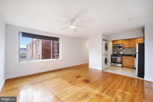 unfurnished living room featuring light wood-type flooring, stacked washer and dryer, and ceiling fan