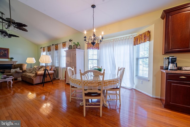 dining space featuring ceiling fan with notable chandelier, vaulted ceiling, and light hardwood / wood-style flooring