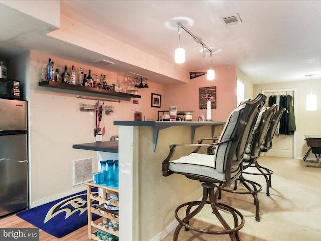 bar featuring hanging light fixtures and stainless steel refrigerator