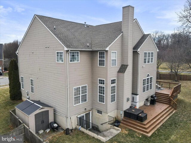 rear view of house featuring a wooden deck, a lawn, and a storage unit