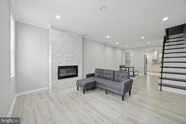 living room with light wood-type flooring, a stone fireplace, and ornamental molding