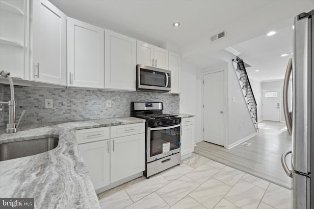 kitchen with sink, light hardwood / wood-style flooring, appliances with stainless steel finishes, light stone counters, and white cabinetry