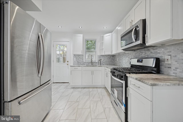 kitchen with light stone countertops, tasteful backsplash, stainless steel appliances, sink, and white cabinetry