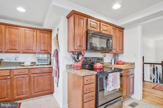 kitchen with black appliances, light hardwood / wood-style floors, and light stone counters