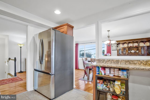 kitchen with stainless steel fridge, light stone counters, decorative light fixtures, an inviting chandelier, and light hardwood / wood-style floors