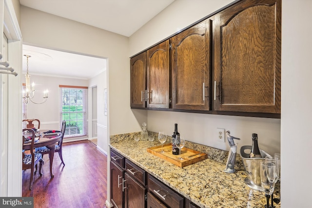 kitchen with a chandelier, dark brown cabinets, dark wood-type flooring, and light stone counters