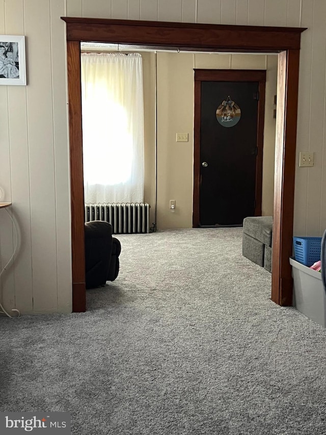 hallway featuring carpet flooring, wooden walls, and radiator heating unit