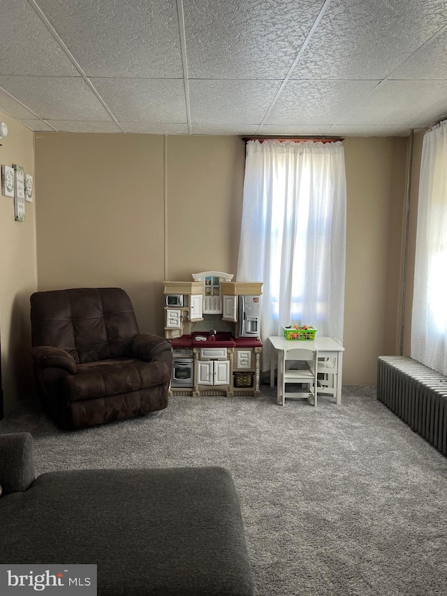 carpeted living room featuring radiator and a drop ceiling