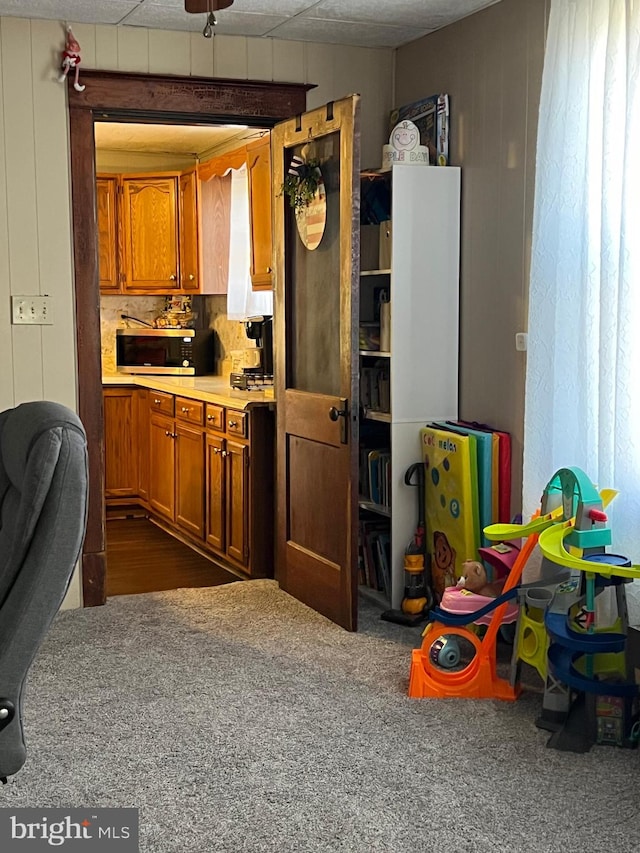 kitchen featuring wood walls, ceiling fan, dark carpet, and backsplash