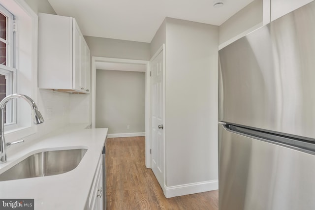 kitchen featuring stainless steel fridge, sink, white cabinets, and light hardwood / wood-style flooring