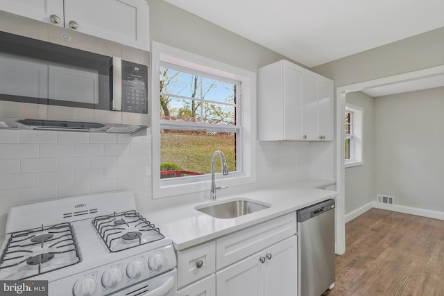 kitchen with sink, light wood-type flooring, tasteful backsplash, white cabinetry, and stainless steel appliances