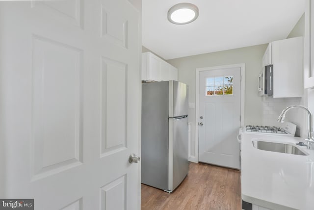 kitchen with backsplash, sink, appliances with stainless steel finishes, light hardwood / wood-style floors, and white cabinetry