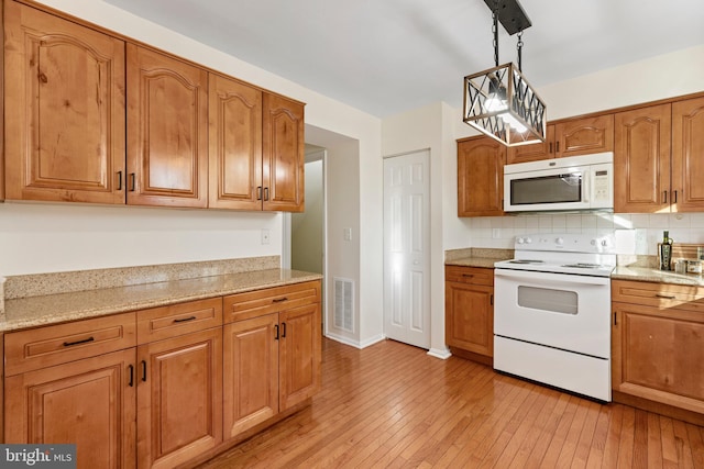 kitchen featuring light wood-type flooring, white appliances, decorative light fixtures, and light stone counters