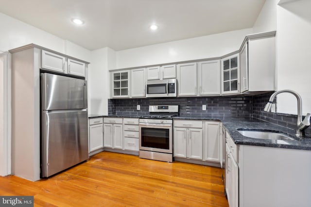 kitchen with light wood-type flooring, backsplash, stainless steel appliances, sink, and dark stone countertops