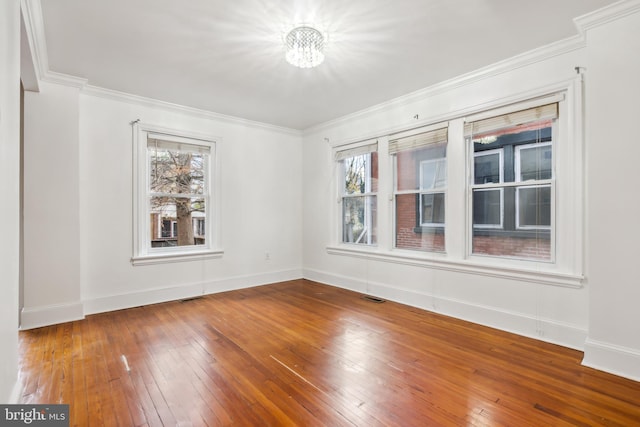 spare room featuring a chandelier, hardwood / wood-style flooring, plenty of natural light, and ornamental molding