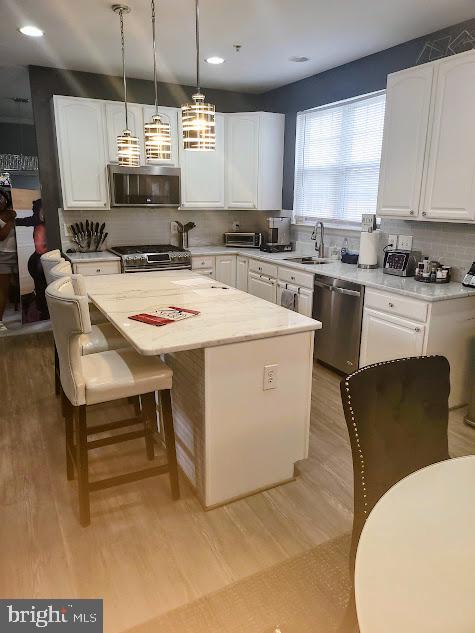 kitchen featuring white cabinets, a center island, stainless steel appliances, and hanging light fixtures