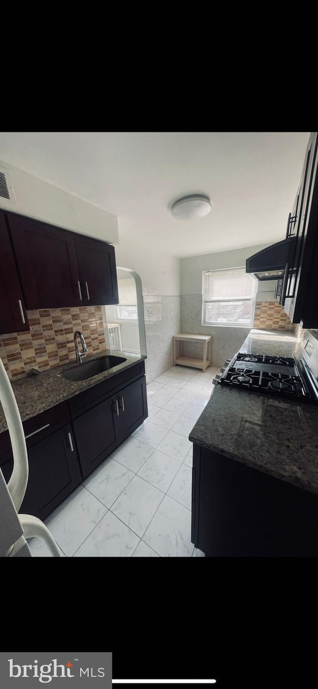 kitchen featuring black gas range, decorative backsplash, sink, and dark stone counters