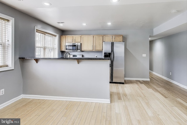 kitchen featuring kitchen peninsula, a breakfast bar area, light brown cabinetry, appliances with stainless steel finishes, and light wood-type flooring