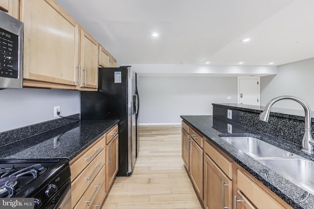 kitchen featuring dark stone countertops, light hardwood / wood-style flooring, stainless steel appliances, and sink