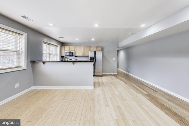 kitchen with kitchen peninsula, light brown cabinetry, stainless steel appliances, and light hardwood / wood-style flooring