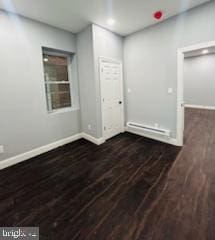 empty room with baseboard heating and dark wood-type flooring