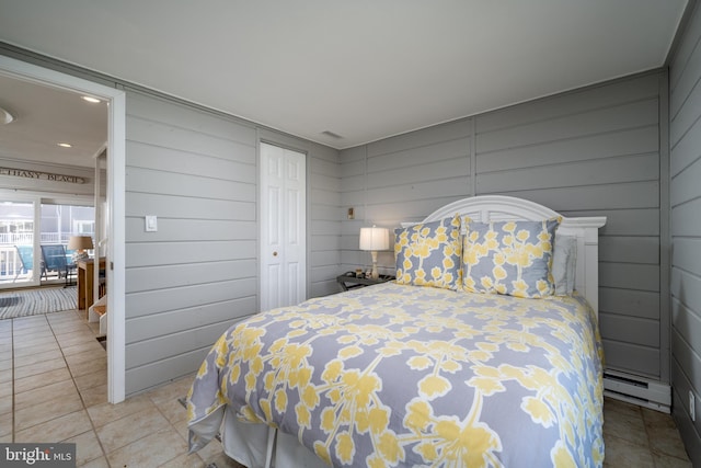 bedroom featuring wood walls, light tile patterned floors, and a baseboard heating unit