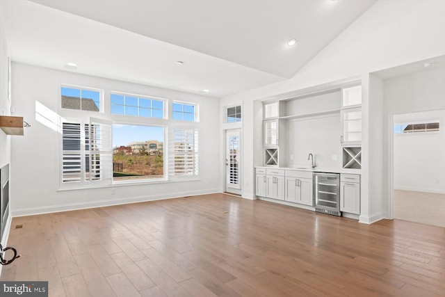 unfurnished living room featuring light hardwood / wood-style floors, high vaulted ceiling, beverage cooler, and indoor wet bar