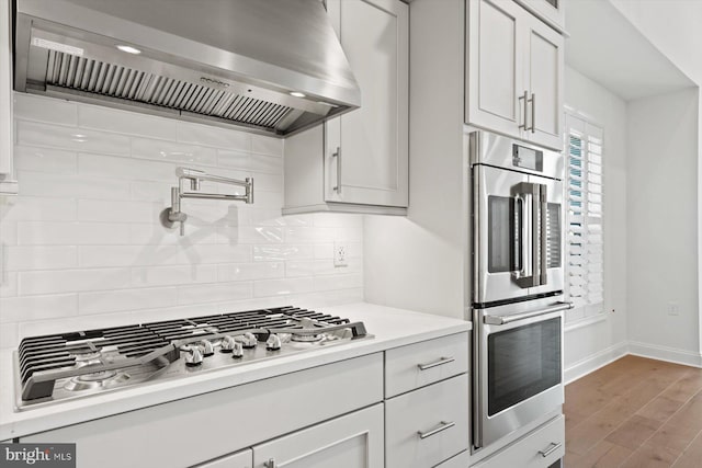 kitchen with appliances with stainless steel finishes, backsplash, wall chimney exhaust hood, white cabinets, and hardwood / wood-style floors