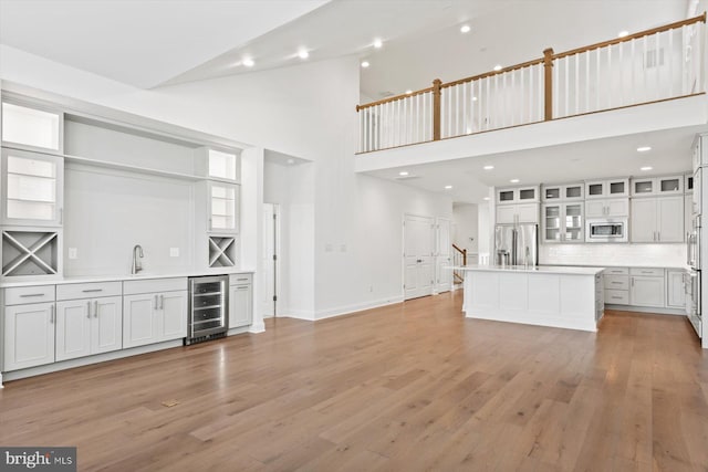 unfurnished living room with high vaulted ceiling, light wood-type flooring, sink, and wine cooler