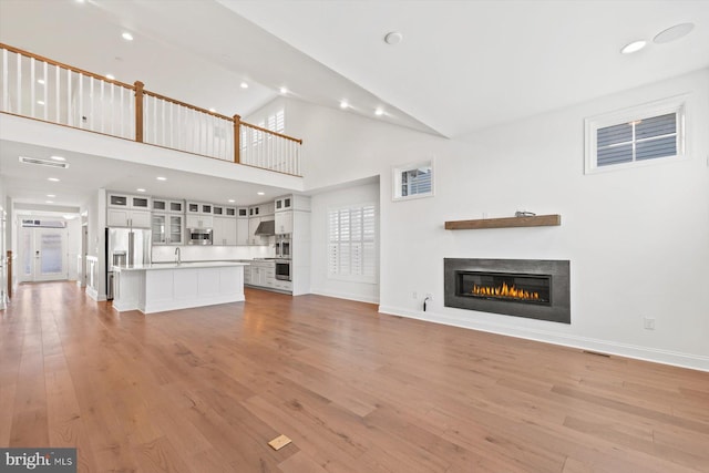 unfurnished living room with sink, high vaulted ceiling, and light hardwood / wood-style flooring