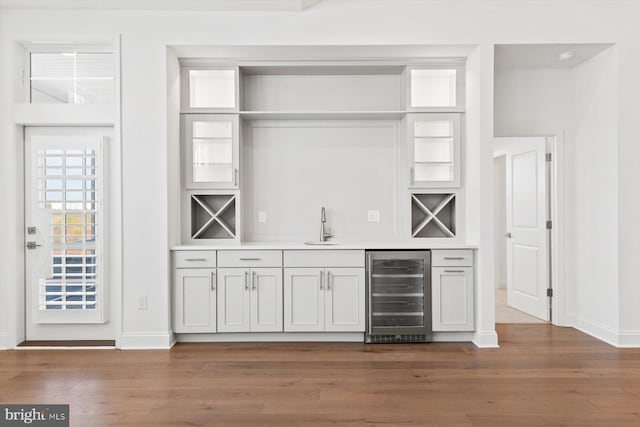 bar with white cabinets, beverage cooler, dark wood-type flooring, and sink