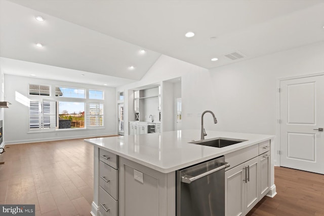 kitchen featuring light wood-type flooring, vaulted ceiling, a kitchen island with sink, sink, and dishwasher