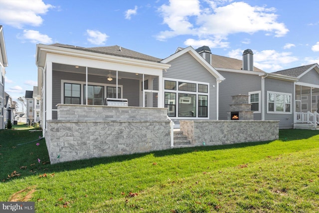 rear view of house featuring an outdoor stone fireplace, a yard, and a sunroom