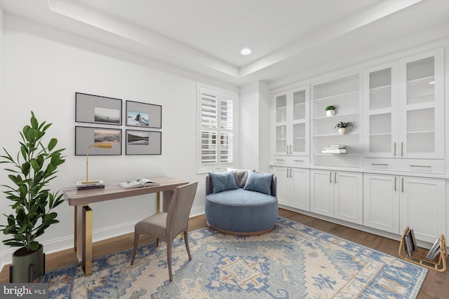 office area with dark hardwood / wood-style flooring and a raised ceiling