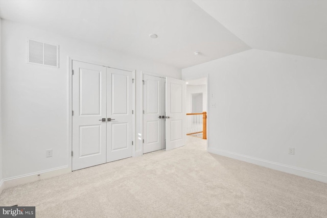 unfurnished bedroom with two closets, light colored carpet, and lofted ceiling